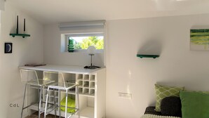Ett litet rum med ett vitt skrivbord, en stol, ett litet fönster och en grön soffa.