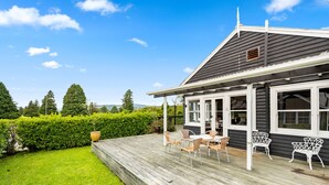 A house with a wooden deck, white chairs, and a garden.