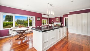A modern kitchen with a large island, white cabinetry, and a view of greenery outside.