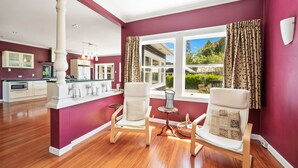 A spacious living area with a large window, a kitchen in the background, and a wooden floor.