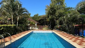 Une piscine rectangulaire bordée de carreaux, entourée de palmiers et d’une clôture.