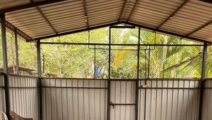 Une table de ping-pong avec un filet, des chaises et un espace abrité, délimité par une clôture en métal et agrémenté de verdure en arrière-plan.