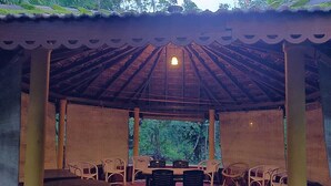 Un pavillon en plein air, doté d’un toit en tuiles, entouré de chaises et de tables, et offrant une vue sur la forêt.