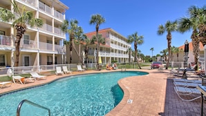 Un hotel con piscina, palmeras y un patio de ladrillo con sillones de descanso.