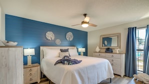 Un dormitorio con cama, mesitas de noche, cómoda, ventilador de techo y decoración mural.