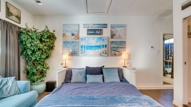 A bedroom with a large bed, a blue sofa, a potted plant, and artwork on the wall. - Pet-Friendly Getaway w/ Projector in Lake Dallas! (Lake Dallas)