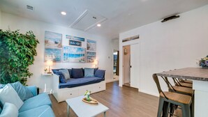 A modern living room with a blue sofa, a small white table, and a kitchen area with a bar stool. - Pet-Friendly Getaway w/ Projector in Lake Dallas! (Lake Dallas)