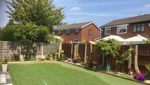A backyard with artificial grass, a green plastic chair, and a black outdoor table with a glass. - Welcome to Your Stay at The Nest (Bolton)
