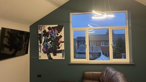 A room with a large window, a ceiling light, and a brown leather couch. - Welcome to Your Stay at The Nest (Bolton)