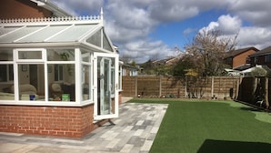 A conservatory with a brick exterior and large glass doors, a paved patio, and a well-maintained lawn. - Welcome to Your Stay at The Nest (Bolton)