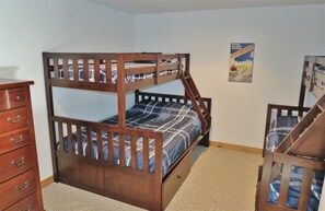 Uma cama beliche com estrutura de madeira, uma cômoda com gavetas e um pôster na parede.