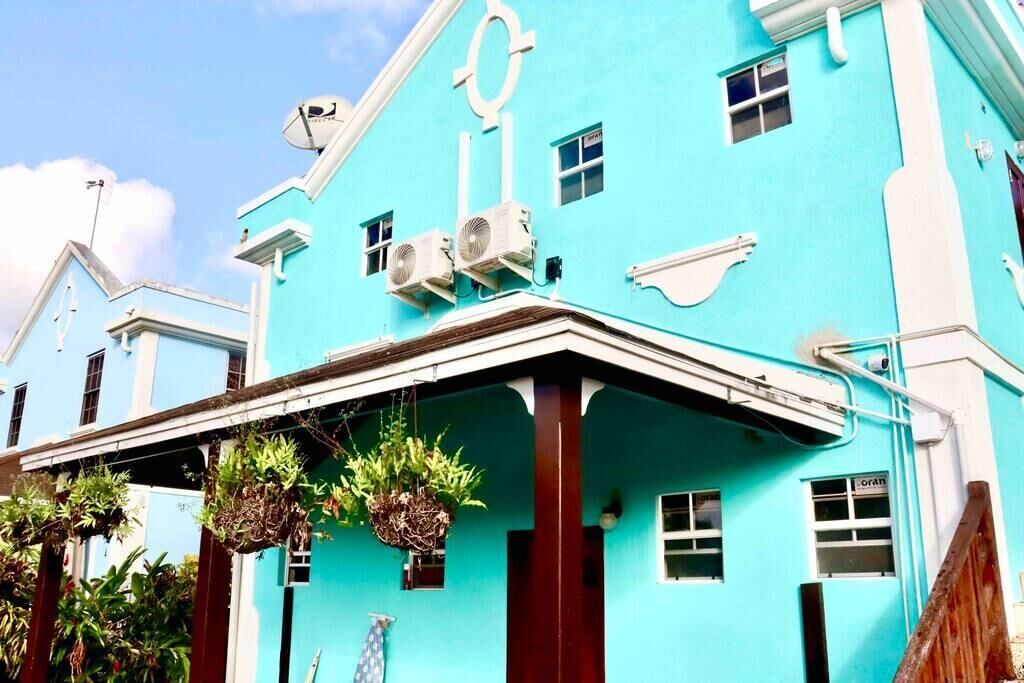 Un bâtiment de couleur turquoise, doté de deux unités de climatisation, d’une antenne parabolique et de plantes suspendues.