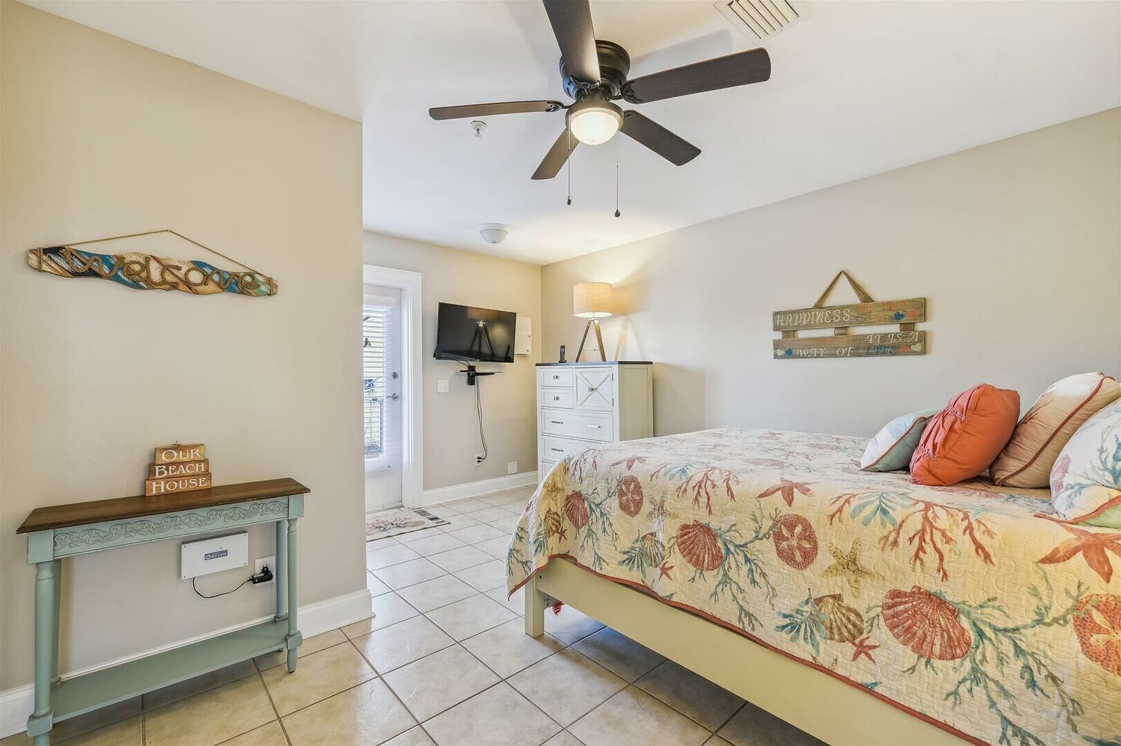 A bedroom with a bed, a ceiling fan, a TV, a dresser, and a wall-mounted shelf.
