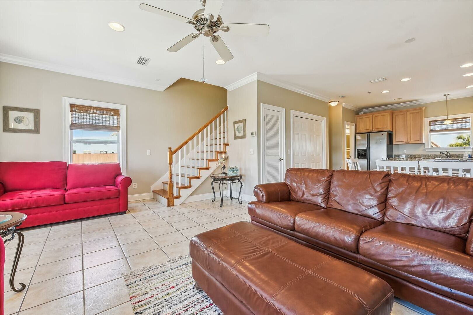 A living room with a red sofa, a brown leather sofa, a ceiling fan, and a kitchen in the background.