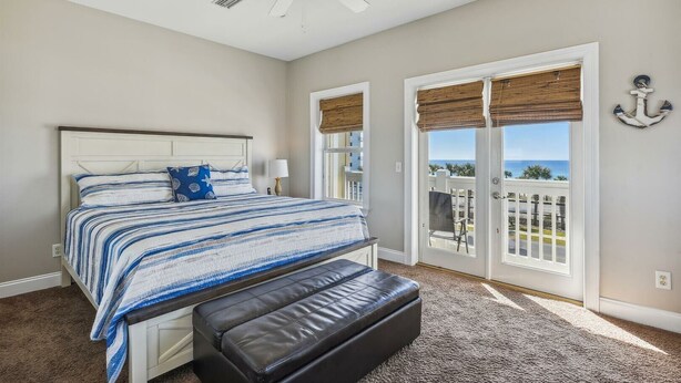 A bedroom with a large bed, a ceiling fan, and a view of the ocean through the windows.