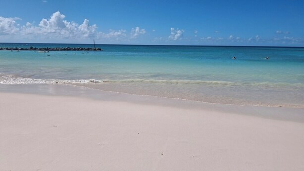 Ein Strand mit klarem türkisblauem Wasser, einem Sandstrand und ein paar badenden Personen.