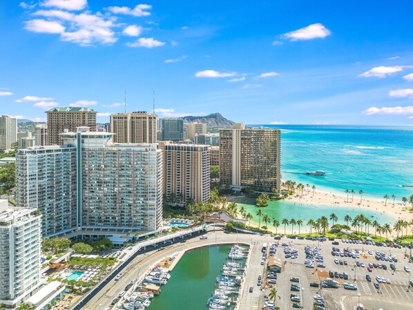 A high-rise hotel with multiple floors, a marina with boats, and a beach with palm trees. - Splendid 2BD w/ One FREE Parking (Honolulu)