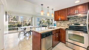 A modern kitchen with a dishwasher, oven, and a large island with a sink. There are pendant lights above the island and a view of a balcony with outdoor seating. - Splendid 2BD w/ One FREE Parking (Honolulu)
