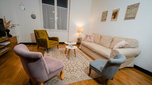 Ein Wohnzimmer mit einer Couch, zwei Sesseln, einem Couchtisch, einer Lampe und einem Fernseher auf Holzboden.