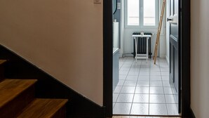Ein Flur mit einer Holztreppe, die zu einem Raum mit Heizkörper und einer an der Wand stehenden Leiter führt.