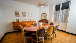 Ein Esszimmer mit Holztisch, sechs Stühlen, einer Chandelüster, einem Spiegel und einem Fenster mit Vorhängen.