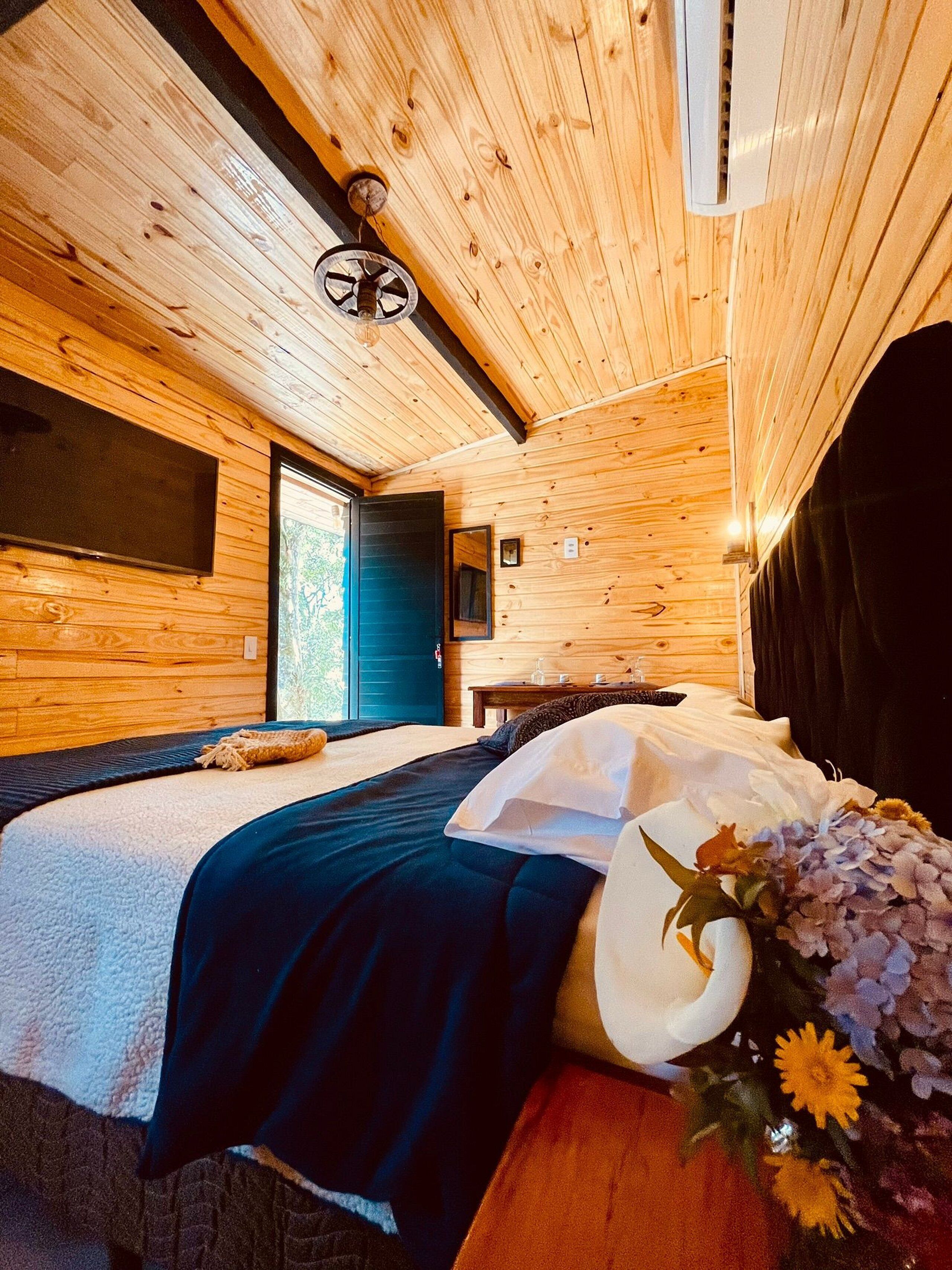 A wooden cabin room with a bed, a small table, and a window.