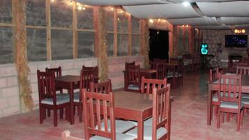 Restaurante com mesas e cadeiras de madeira, parede de tijolos e uma grande janela.