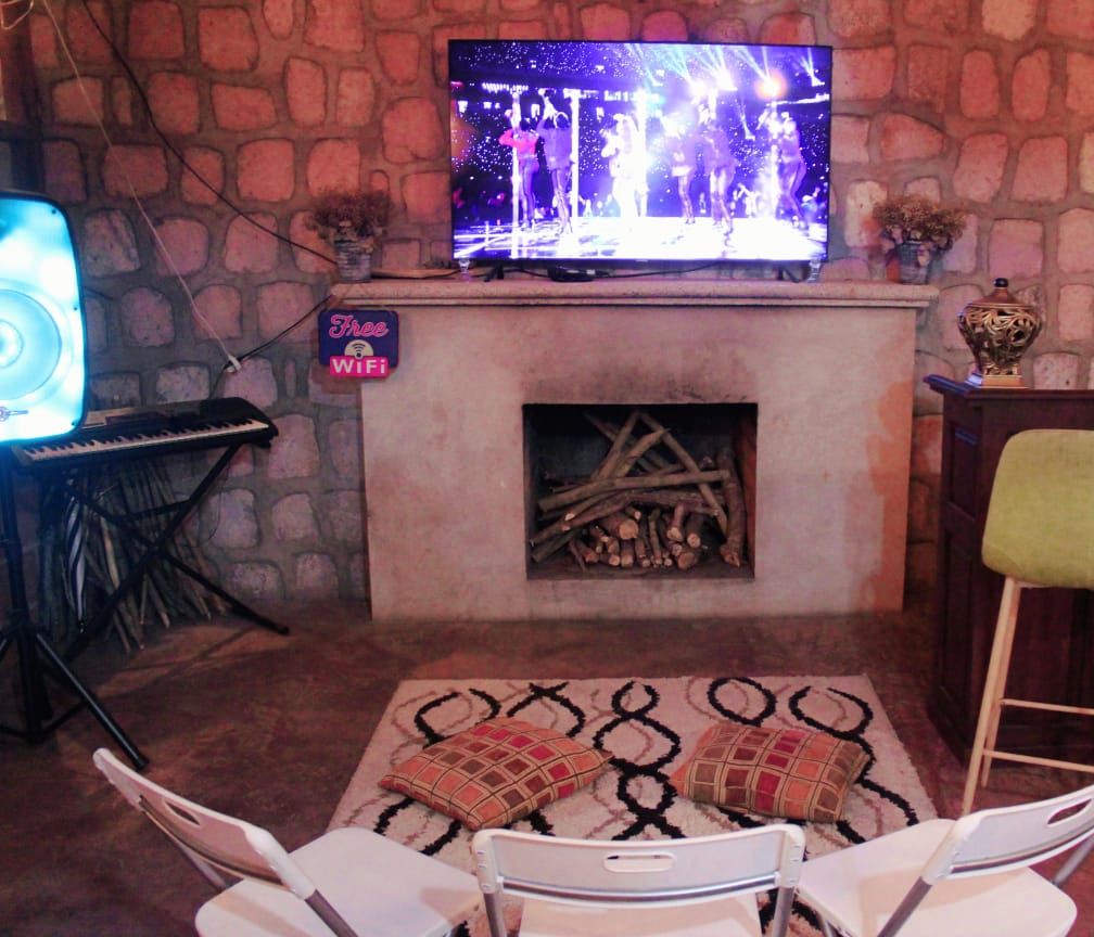 Una sala de estar acogedora con una pared de piedra, una chimenea, un televisor y dos taburetes de bar.