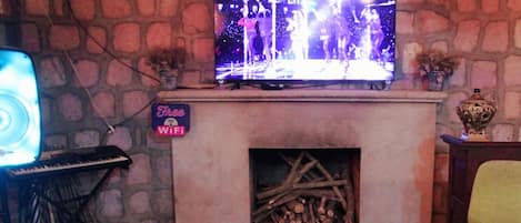 Uma sala de estar aconchegante com parede de pedra, lareira, televisão e dois bancos altos.