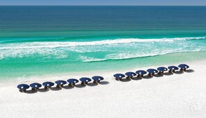 A beach with white sand and a row of blue umbrellas.