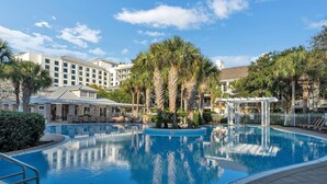 A swimming pool with lounge chairs and palm trees, surrounded by hotel buildings.