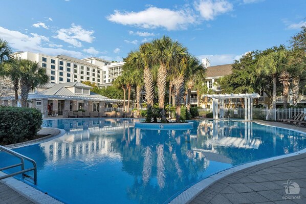 A swimming pool with lounge chairs and palm trees, surrounded by hotel buildings.
