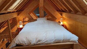 A high-ceilinged attic bedroom with a large bed, wooden beams, and two bedside lamps. - 2nd floor, tv, ski locker, 78m², Serre Chevalier (Le Monêtier-les-Bains)