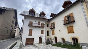 A courtyard with a white building featuring wooden shutters, a stone-paved area, and a small garden. - 2nd floor, tv, ski locker, 78m², Serre Chevalier (Le Monêtier-les-Bains)