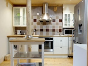 Kitchen features a stainless steel range hood, oven, microwave, and refrigerator, along with white cabinetry and a wooden table.