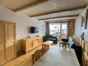 Cozy living space with a dining table, sofa, and TV, featuring a rustic wooden ceiling and a window.
