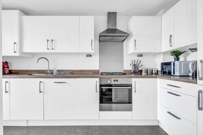 Una cocina moderna con armarios blancos, una campana de acero inoxidable y un horno empotrado.