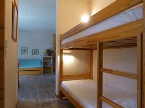 Kerrossängyllä varustettu huone, jossa on puinen sängynrunko, pieni yöpöytä lampun kanssa ja sininen päiväpeite.