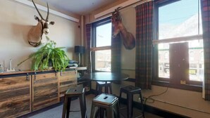 A room with a wooden cabinet, a potted plant, a table with stools, and two mounted animal heads. - Benson Lodge Room -2 (Silverton)