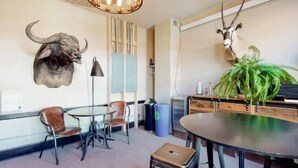 A room with a round table, two chairs, a trash bin, and two mounted animal heads on the wall. - Benson Lodge Room -2 (Silverton)