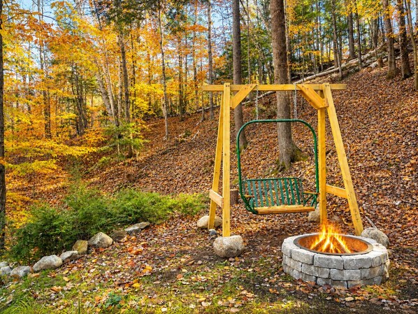 A swing set with a fire pit in a wooded area. - Beautiful Chalet 2 minutes from the Saco River 🚣🔥🌲🗻 (Bartlett)