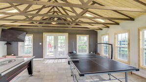 Ein Tischtennis-Tisch in einem Raum mit schräg verlaufender Decke, großen Fenstern und einer Tür, die nach draußen führt.