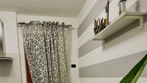 A modern kitchen with a dining area, featuring a white and gray striped wall, a patterned curtain, and a plant on the table. - Vacation home ACCIUGA (Monterosso al Mare)