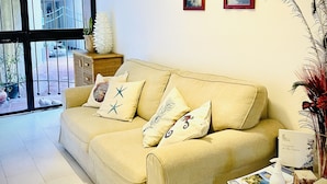 A living room with a beige sofa, two framed pictures, a vase with dried plants, and a table with a book and a bottle. - Vacation home ACCIUGA (Monterosso al Mare)