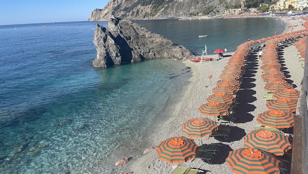 A coastal beach with clear waters, rocky outcrops, and a row of striped beach umbrellas. - Vacation home ACCIUGA (Monterosso al Mare)