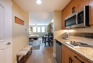 A modern kitchen with a built-in microwave, stove, and dishwasher. There is a dining area with a table and chairs, and a bench along the hallway.