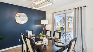A dining area with a dark blue wall, a round mirror, a hanging light fixture, and a table set for six with chairs. - Baberville By Book That Condo (Panama City Beach)