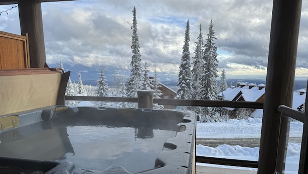 A hot tub with a view of snow-covered trees and houses.