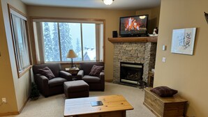 A cozy living room with a stone fireplace, a television, and comfortable seating.