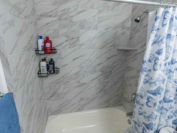 A bathroom with a bathtub, shower curtain with butterfly pattern, marble tiles, and toiletries on shelves.